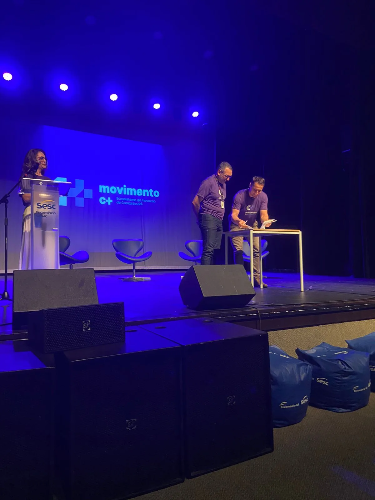 Mesa de assinaturas no palco do Movimento C+ com identificação Sesc no cenário.