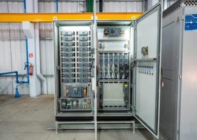 Montagem interna de painel elétrico industrial aberto, com equipamentos, bornes e fiacao em organização de fábrica.