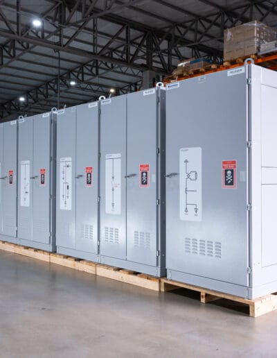 Perspectiva de fileira de painéis elétricos industriais em ambiente de galpão.